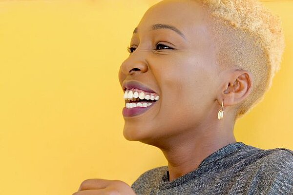 A smiling black woman with short blonde hair, against a yellow background